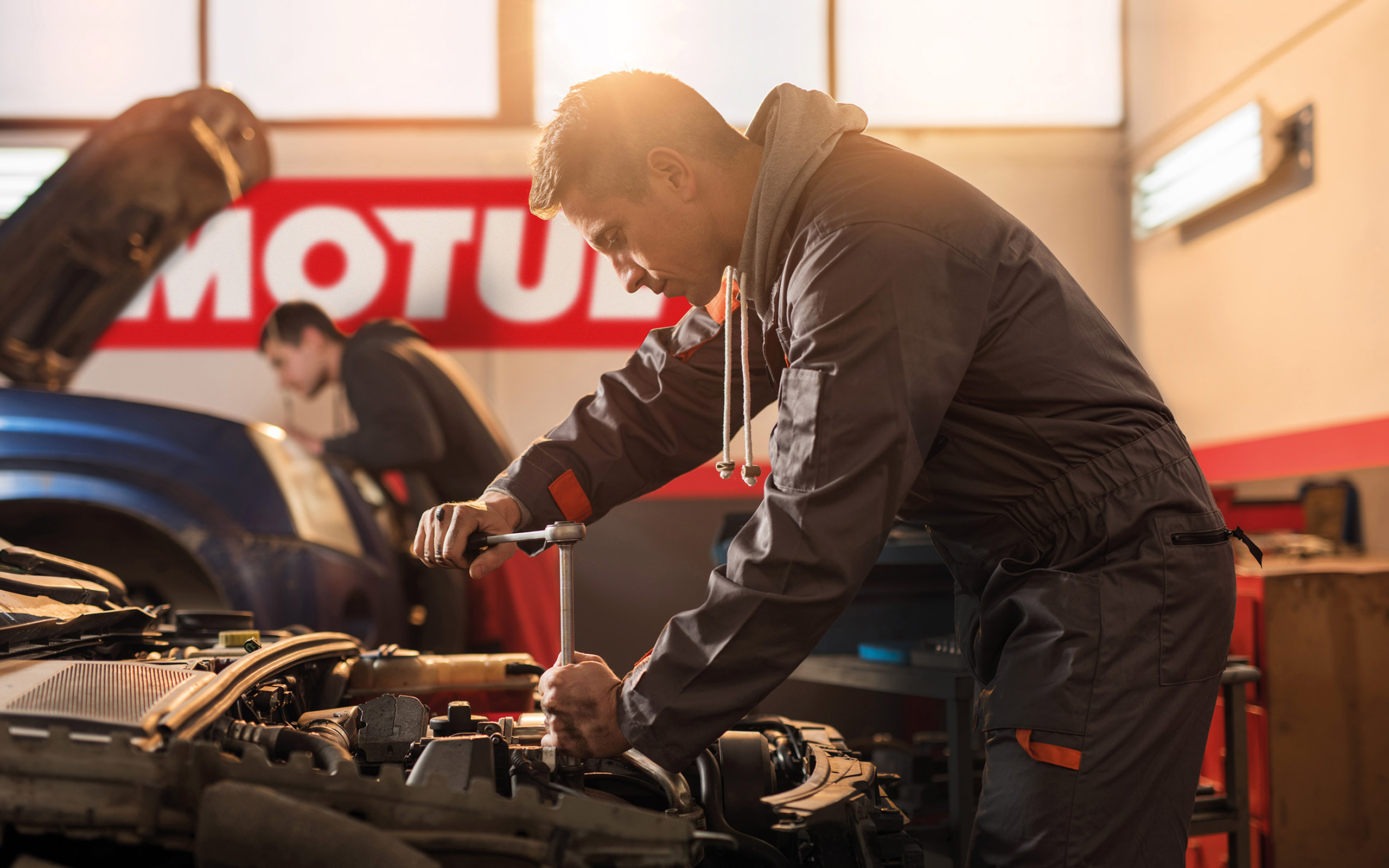 Mechanic working on an engine in front of a Motul banner